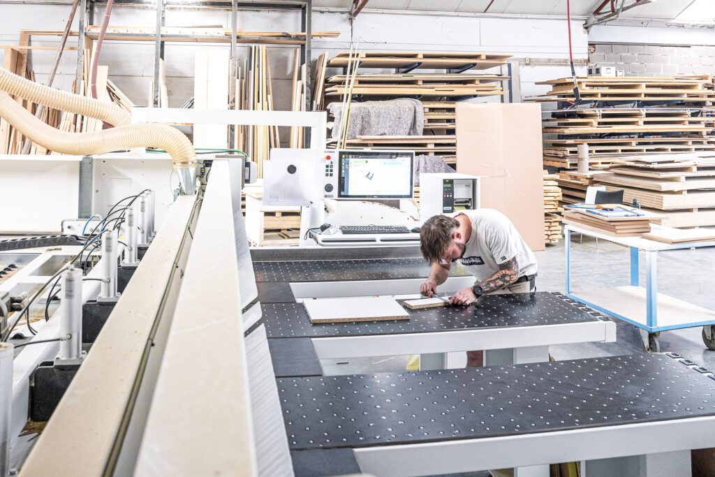 Craftsman inspecting a wood panel on a CNC woodworking machine at La Menuiserie's workshop Copier
