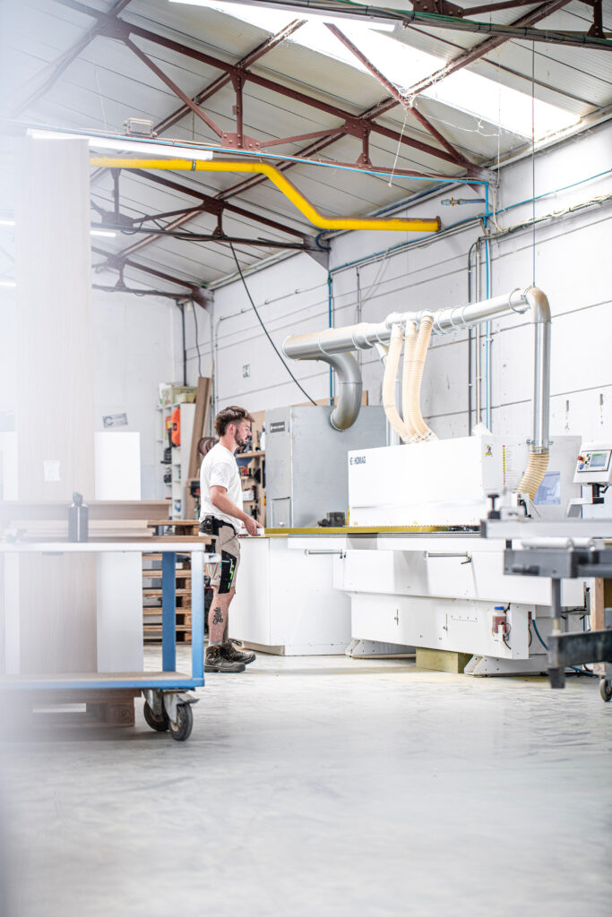 Craftsman operating industrial woodworking machinery in La Menuiserie's production workshop Copier