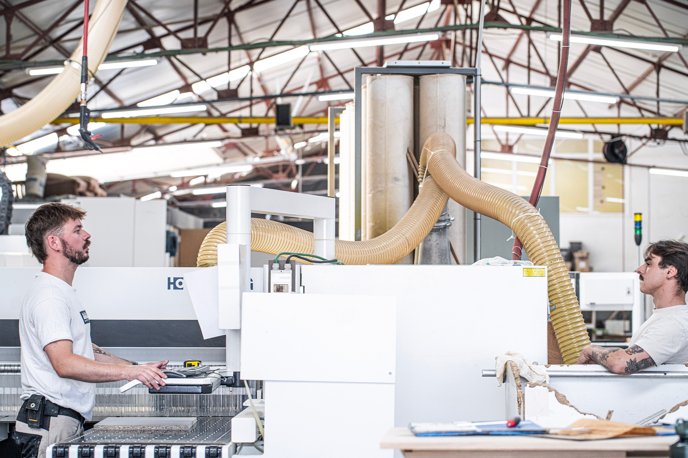 Two craftsmen operating industrial woodworking machinery at La Menuiserie's workshop Copier