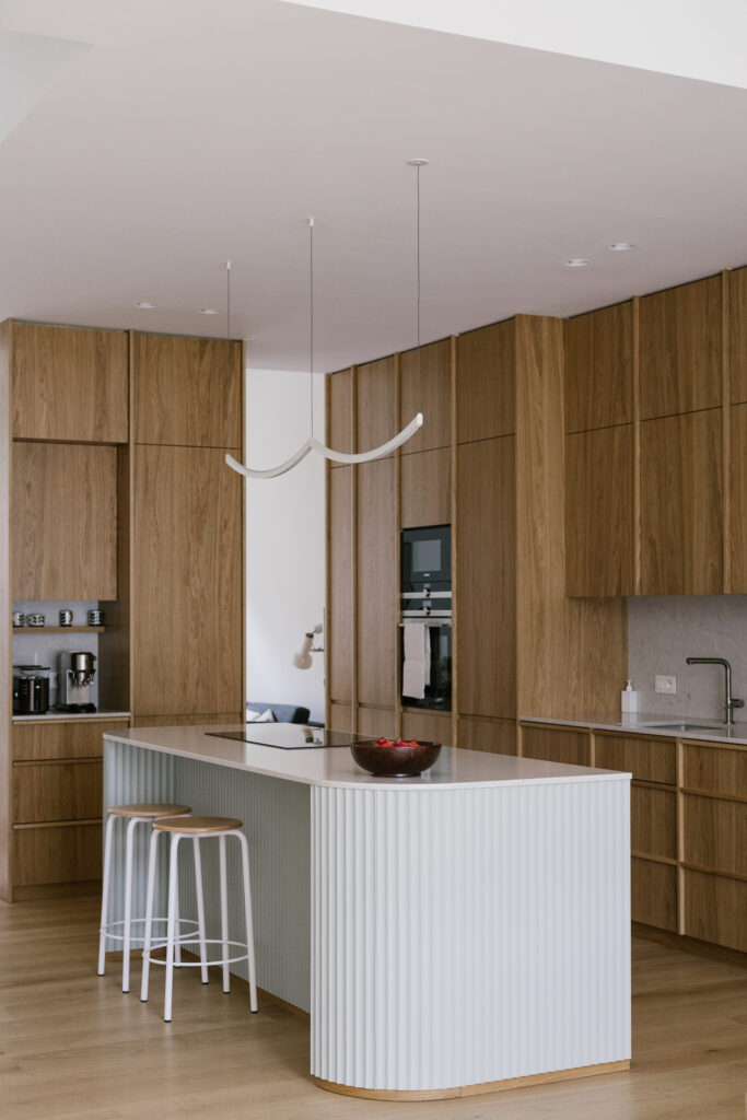 Contemporary bespoke oak kitchen with curved fluted island, integrated appliances and breakfast stools