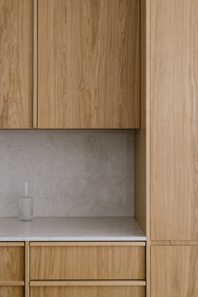 Bespoke oak kitchen cabinetry with handleless doors and grey stone backsplash Copier