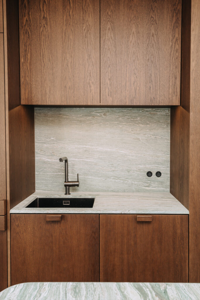 Bespoke dark wood kitchen cabinetry with black sink and green natural stone backsplash Copier