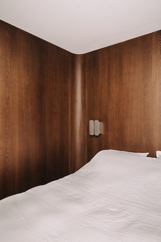 Bespoke dark wood wall panelling with curved corner and integrated bedside lighting Copier