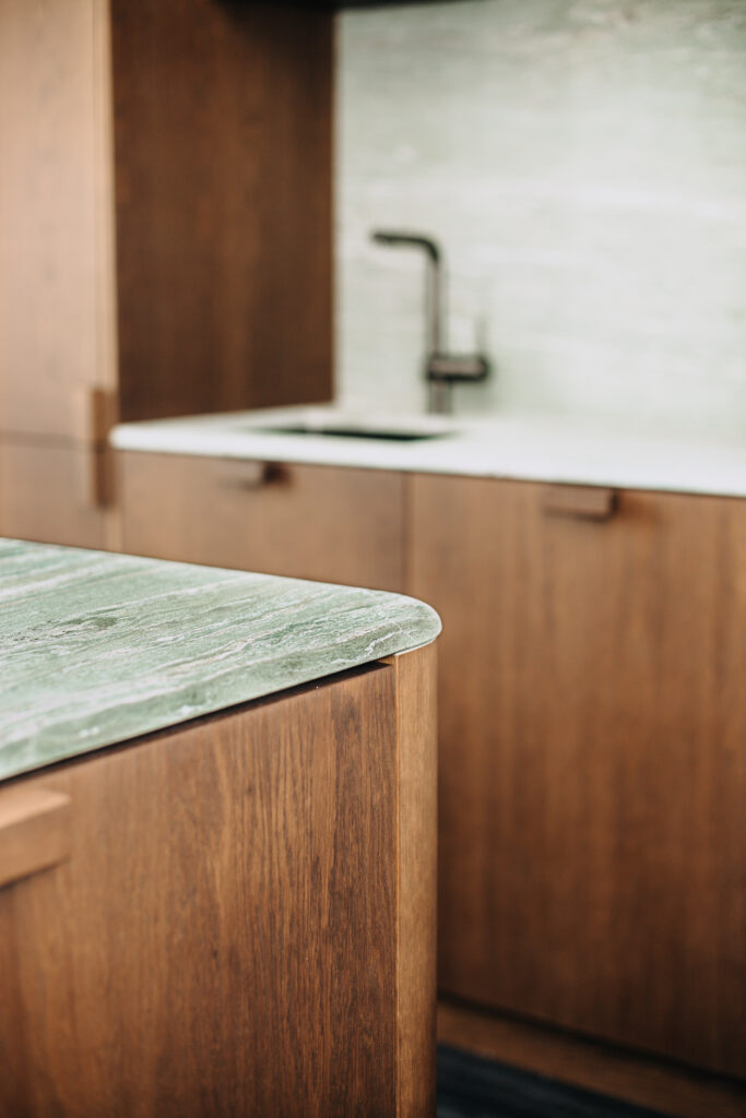 Close-up of a bespoke wooden kitchen island with rounded green stone countertop Copier