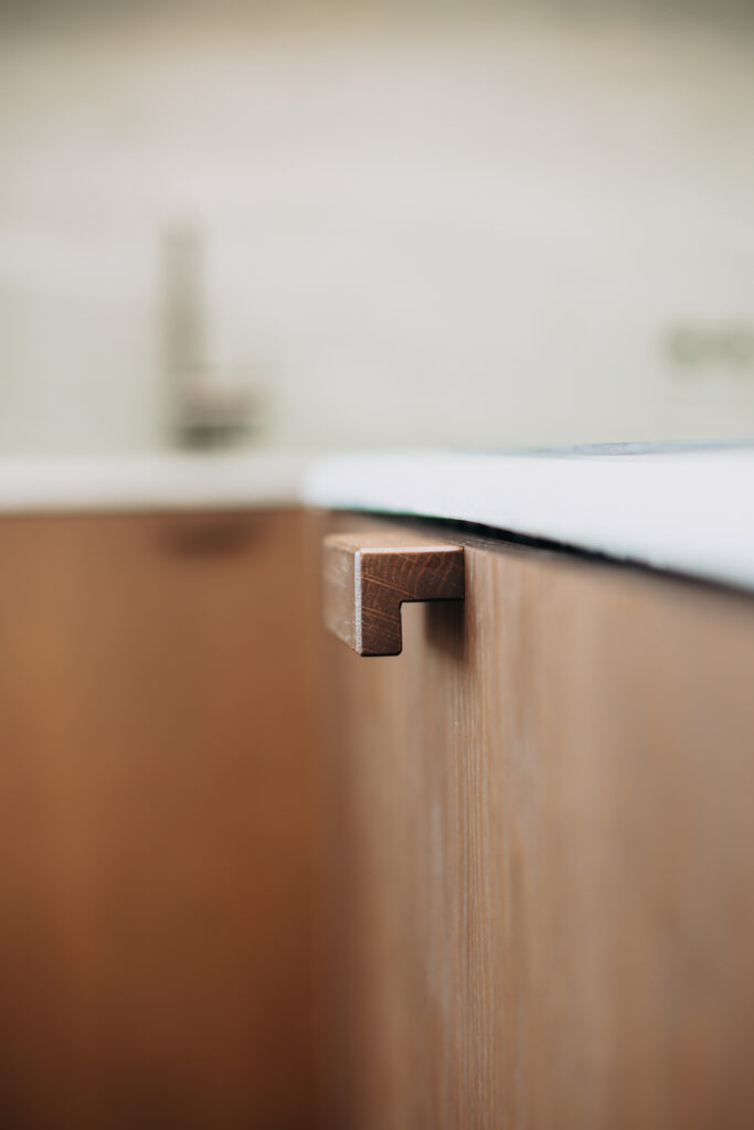 Close-up of a bespoke wooden cabinet handle beneath a stone kitchen countertop Copier