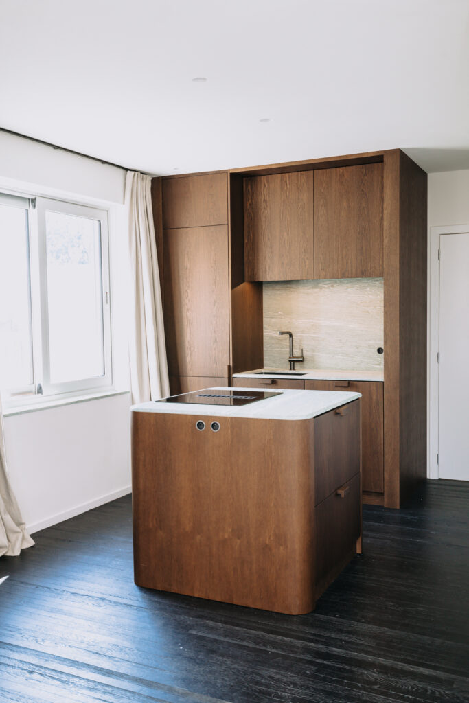 Bespoke dark wood kitchen with rounded island, light stone countertops and black timber flooring Copier